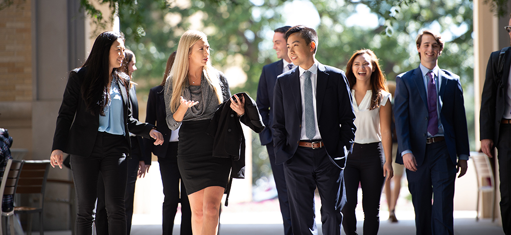 Section Image: A group of students in suits walking, talking with each other and laughing. 