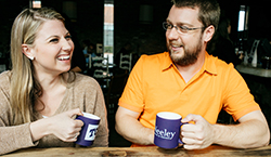 A man and a woman with Neeley coffee mugs sit together at a table