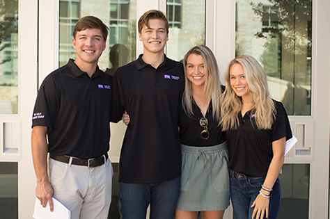 Four Neeley Leadership students standing with arms around each others shoulder at the door to the business school.