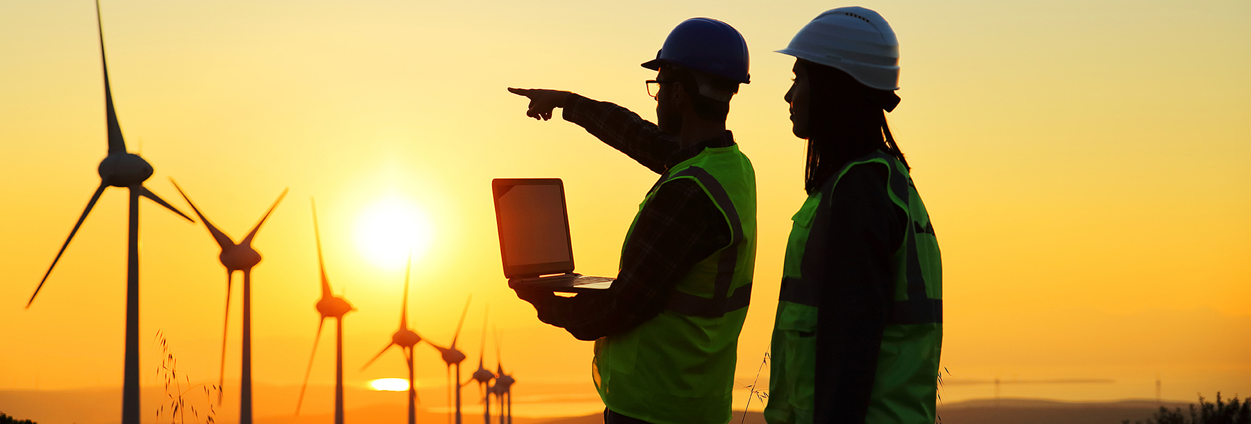 Section Image: Men with laptop observing windmills at sunset 