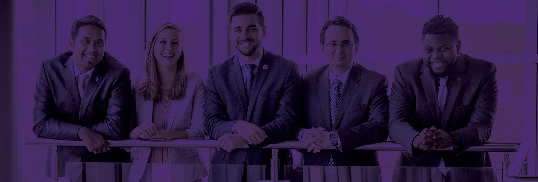 Section Image: TCU Students smiling and wearing suits leaning against the railing in the Rogers Rotunda. 