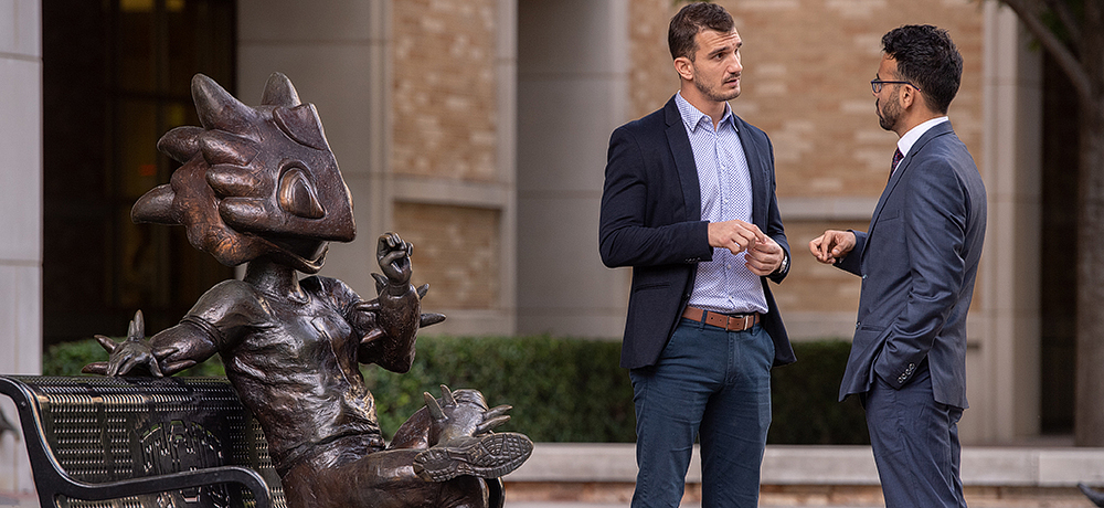 Two men talking by statue of Superfrog on a bench