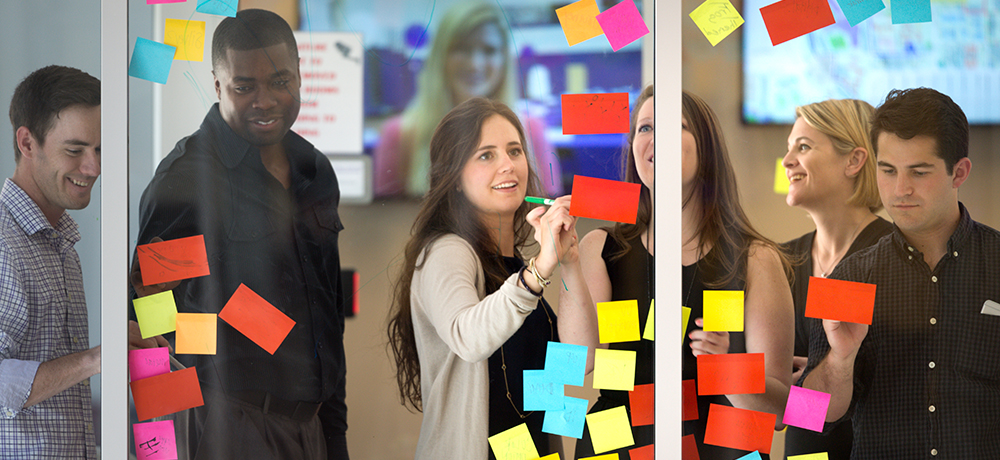 Students writing on Post-it notes on the glass wall of a classroom