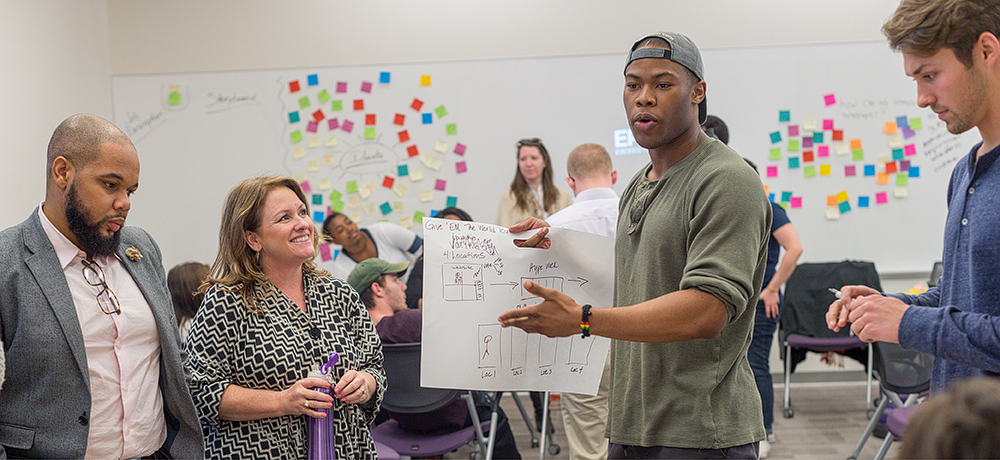 Section Image: Student with chart presents ideas to a group. 