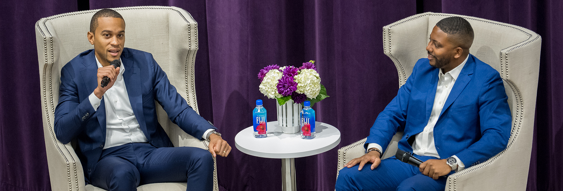 Section Image: Sekou Lewis and David Russell sit on the stage with microphones at the event. 