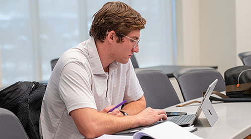 Male student in a classroom on his laptop