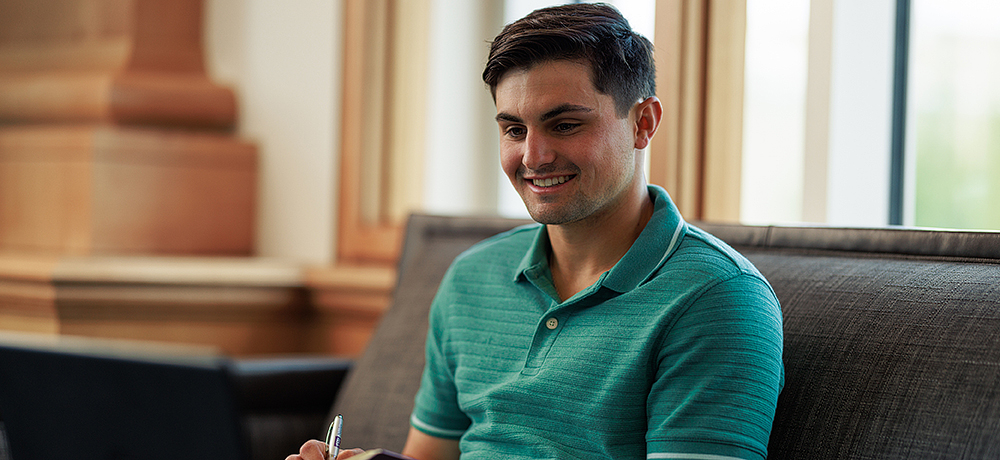 Section Image: Student in a green shirt sits on a couch with pen and paper 