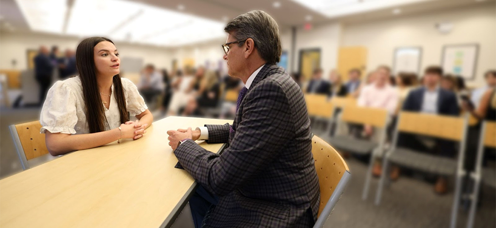 Section Image: Female student sitting across the table from a competition judge. 