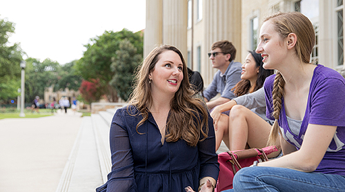 Students sit on the steps of the library and converse