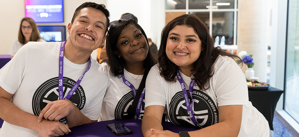 Three program participants in program t-shirts and wearing lanyards smile at the camera