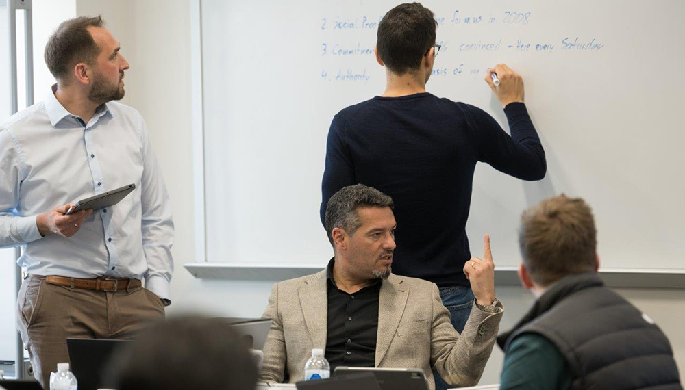 Students in classroom watching someone write on a whiteboard