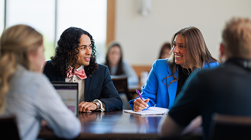 Section Image: Students at a table looking at each other 