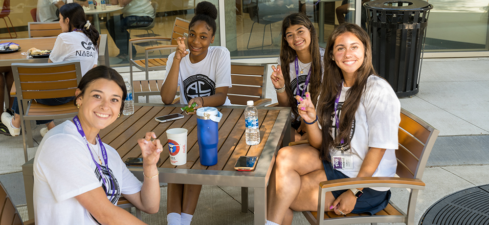 Four girls sitting at a table outside Smith Hall with drinks and food.