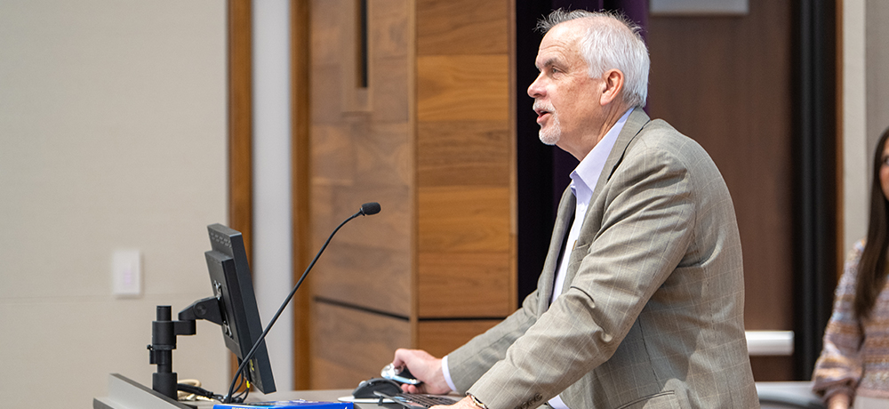 Professor Cliff Defee speaking from the lectern in Shaddock Auditorium.