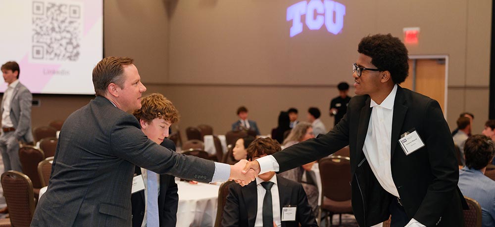 Mentor and student shaking hands across a table in the BLUU ballroom