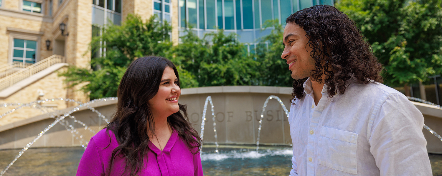Two students talking in front of the building fountain area